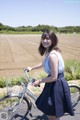 A woman standing next to a bike in a field.