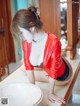 A woman in a red leather jacket and black panties kneeling on a counter.