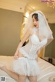 A woman in a wedding dress sitting on a bed.