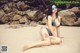 A woman in a bikini sitting on a beach.