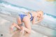 A woman in a bikini kneeling on the beach.