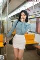 A woman in a blue top and white skirt on a subway train.