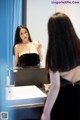 A woman in a black dress looking at herself in the mirror.