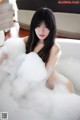 A woman sitting in a bathtub filled with foam.