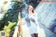 A woman in a white dress and fur coat standing on a wooden bridge.