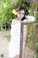 A woman in a white dress leaning against a fence.