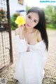 A woman in a white dress holding a yellow flower.