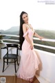 A woman in a pink dress standing on a balcony.