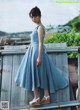 A woman in a blue dress standing on a wooden fence.