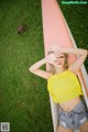 A woman in a yellow top and denim shorts leaning against a surfboard.