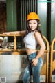 A woman wearing a hard hat leaning against a fence.