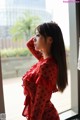 A woman in a red polka dot dress standing by a window.