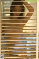 A naked woman standing in front of a window with blinds.