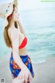 A woman in a red bikini and a straw hat on the beach.