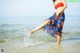 A woman in a red top and blue skirt standing in the water.