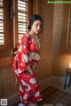 A woman in a red kimono standing in front of a window.