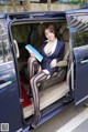 A woman sitting in the back of a blue car holding a book.