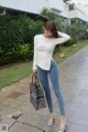 A woman in a white shirt and blue jeans holding a black bag.