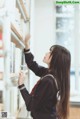 A woman in a school uniform is looking at books on a shelf.