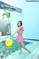 A woman in a pink dress standing in a pool with a yellow ball.