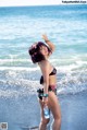 A woman in a bikini standing on a rock by the ocean.