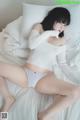 A woman in a white sweater and panties laying on a bed.