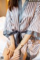 A woman sitting on a bed wearing a striped robe.