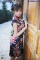 A woman in a cheongsam leaning against a wooden door.