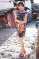 A woman in a black dress standing on a cobblestone street.