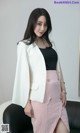 a woman in a white blazer and pink skirt posing for a picture