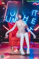 A woman sitting on a red chair in front of a neon sign.