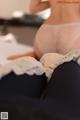 A woman in a white bra and black tights sitting on a bed.