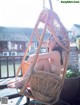 A naked woman sitting in a wicker chair on a balcony.